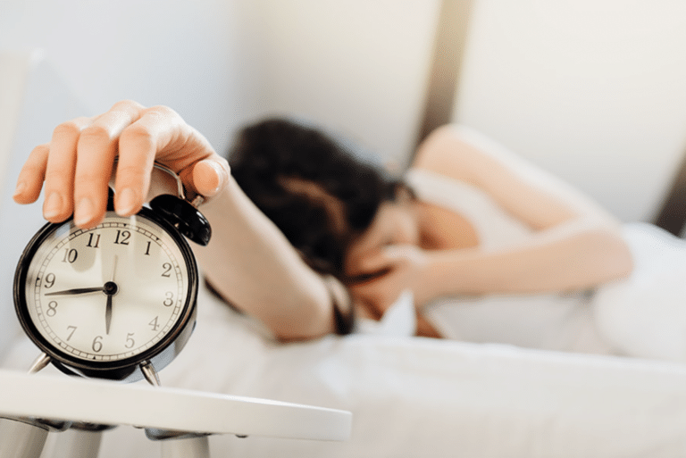 Personne réveillée tenant un réveil illustrant les troubles du sommeil et les solutions naturelles pour mieux dormir