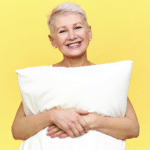 Femme souriante avec un oreiller illustrant les bienfaits du bruit blanc et du bruit rose pour améliorer le sommeil après 60 ans