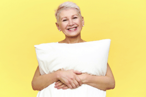 Femme souriante avec un oreiller illustrant les bienfaits du bruit blanc et du bruit rose pour améliorer le sommeil après 60 ans